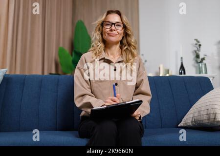 Pleasant mature female psychologist or lawyer sitting on sofa in home office Stock Photo