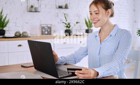 A young happy female in a striped blue shirt using her card to pay for her online shopping cart Stock Photo