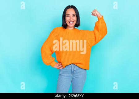 Photo of satisfied glad gorgeous girl straight hairdo dressed orange pullover hand on waist clench fist isolated on teal color background Stock Photo