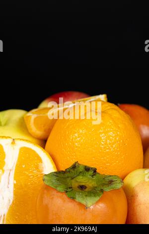 Fruits of orange and yellow colors - apples, persimmons and oranges on a black background Stock Photo