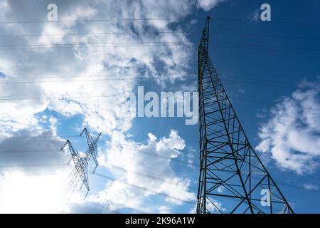 Electricity pylon for transmission and current transfer of high voltage through natural landscapes in front of a cloudy sky Stock Photo