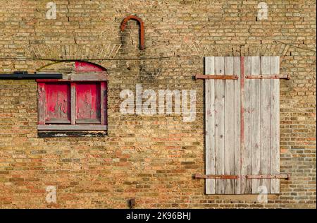 Distressed And Worn Shuttered Window And Door Of A Brick Fronted Old Warehouse Wharf On The Quay Side. King's Lynn UK Stock Photo