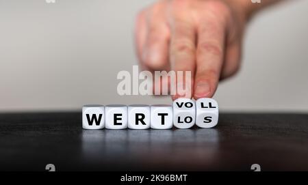 Hand turns dice and changes the German word 'wertlos' (worthless) to 'wertvoll' (valuable). Stock Photo