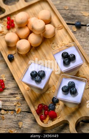 A beautiful shot of white and purple mousse with blueberries and macaroons on a wooden board Stock Photo