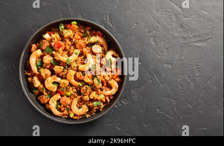 Creole style jambalaya with chicken, smoked sausages and vegetables in pan over black stone background with free text space. Top view, flat lay Stock Photo