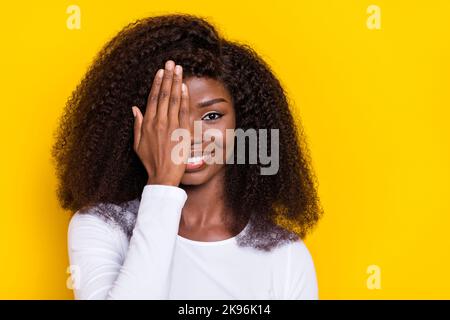 Portrait of satisfied glad person arm palm covering one eye toothy smile isolated on yellow color background Stock Photo