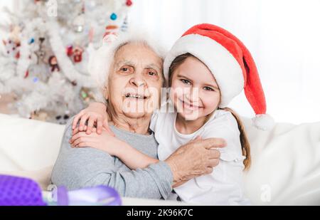 smiling granddaughter in santa hat hugging with grandma Stock Photo