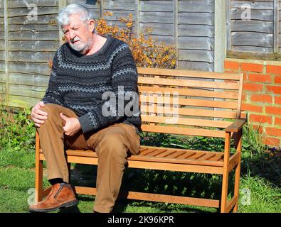 Senior or elderly man suffering pain with arthritis in the knee or leg. Holding his legs in agony. Stock Photo