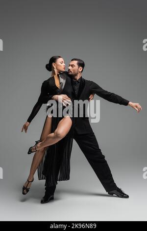 Professional ballroom dancers in black costumes performing tango on grey background Stock Photo