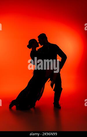Side view of silhouette of couple dancing tango on red background Stock Photo