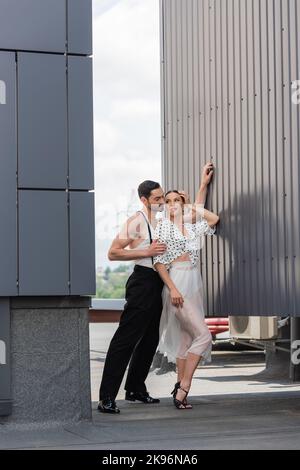 Dancer hugging smiling partner in heels and skirt on rooftop of building at daytime Stock Photo