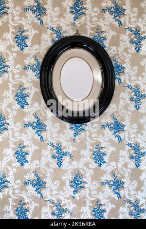 Vintage blank oval picture frame hanging on a wallpaper decorated wall Stock Photo