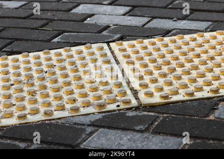 Cobbled street pavement with gray bricks and yellow tactile warning plates Stock Photo