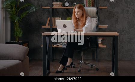 A Caucasian red-haired woman typing on her laptop in a beautifully decorated office. Stock Photo