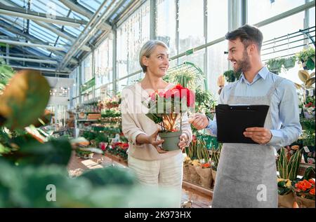 florist seller discussing a beautiful flower with a female guest. Stock Photo
