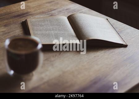 Cup of coffee and opened book. Coffee cup and ancient book on wooden table. Literature concept. Autumn still life. Espresso in library. Stock Photo