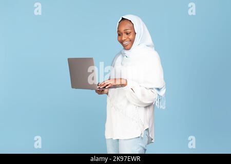 Freelance and online education for muslim women concept. Happy black woman in hijab holding and typing on laptop Stock Photo