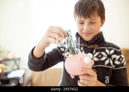 The child will make money. Financial literacy lessons for schoolchildren. the boy collects money for his studies. A happy child puts money in the Stock Photo