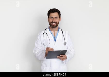 Medical Services. Portrait Of Smiling Handsome Male Doctor In Uniform Holding Clipboard Stock Photo