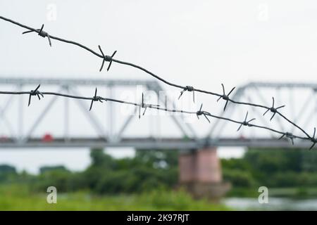 The concept of transport security. Barbed wire on the background of the railway bridge. Railway bridge in blur. Stock Photo