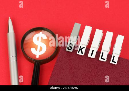 Business concept. On the red surface is a pen, a magnifying glass with a dollar symbol and a notepad with clothespins and the inscription - SKILL Stock Photo