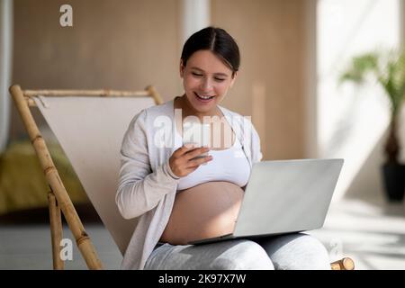 Happy Pregnant Woman Using Mobile Phone And Laptop At Home Stock Photo