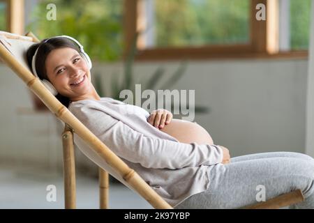 Pregnancy Leisure. Happy Pregnant Woman Listening Music In Wireless Headphones At Home Stock Photo