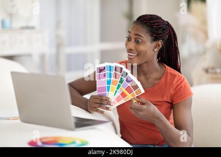 Black Female Interior Designer Using Laptop For Showing Swatches To Client Stock Photo