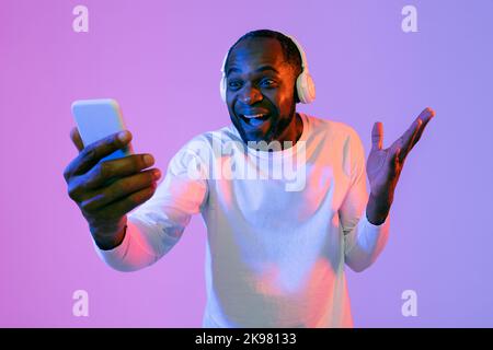 Emotional black man with wireless headset using smartphone Stock Photo