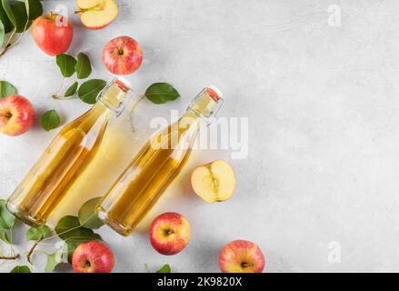 Apple cider vinegar in a two glass bottles and fresh apples with leaves on light background, top view, copy space Stock Photo