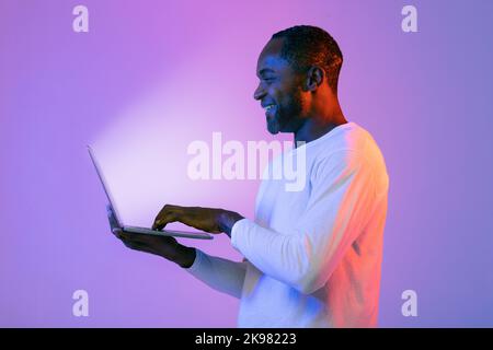 Cheerful black man using modern laptop with shining screen Stock Photo