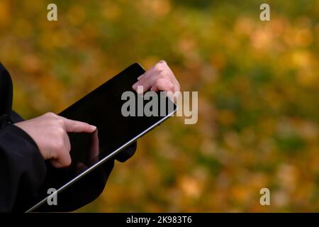 boy with tablet near school with a book online learning, child's hands holding a tablet, touchpad, finger touch on the tablet, working with the tablet Stock Photo