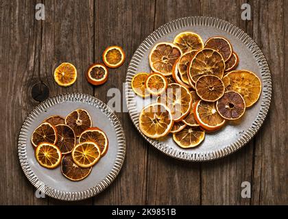 Top view of dried orange slices on ceramic plates with on rustic wooden background. Ingredients for cooking or Christmas decoration. Stock Photo