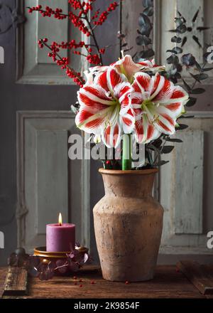 Bouquet with red, white Amaryllis flower, eucalyptus and red holly berry branches, in a ceramic vase and burning candle in a small bowl. Stock Photo
