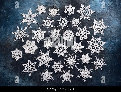 Top view of white cotton crocheted stars and snowflakes on dark blue background. Easy handmade Christmas decoration or small gift. Stock Photo
