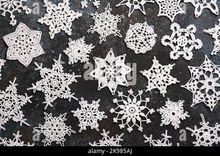 Beautiful varied white cotton crocheted stars and snowflakes on dark background. Easy handmade Christmas decoration or small gift. Flat lay. Stock Photo
