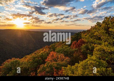 Sun setting behind clouds illuminating the fall colors of the trees in Coopers Rock State Forest Stock Photo