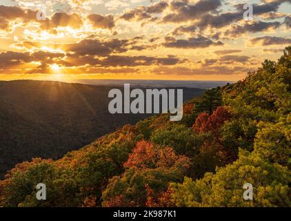 Sun setting behind clouds illuminating the fall colors of the trees in Coopers Rock State Forest Stock Photo