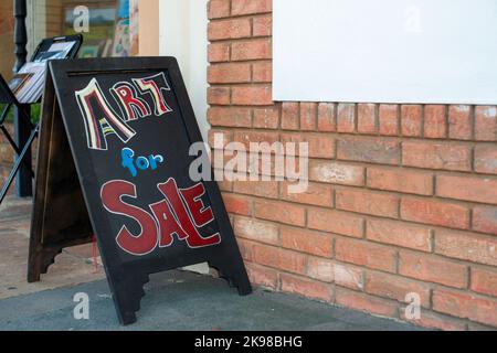 A rectangle shaped black painted wooden A framed sidewalk easel sign with Art for Sale written in colorful red, pink, and blue chalk text. Stock Photo