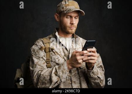 European military man wearing uniform using mobile phone isolated over black background Stock Photo