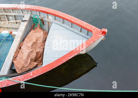 A grey wooden boat, a fishing boat,  with red trim. The motorboat is moored with a green rope. The vessel is reflected in the shallow clear water. Stock Photo