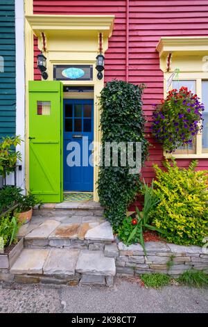 The entrance to a heritage home with a blue wood and glass door and a green wooden shutter door. The exterior wall is red with yellow trim. Stock Photo