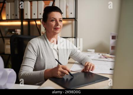 Portrait of smiling mature architect using graphic tablet when drawing new project on computer Stock Photo