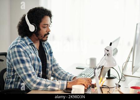 Software developer in plaid shirt listening to music in headphones and coding on laptop Stock Photo