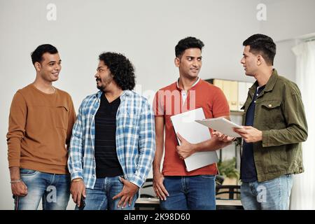 Cheerful start-uppers standing in office, smiling and looking at each other Stock Photo