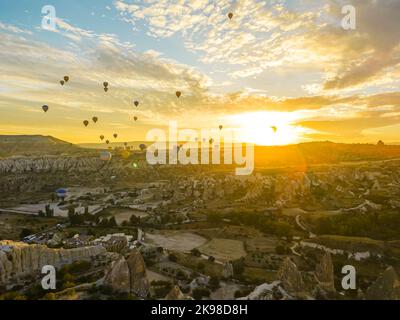 Ballooning concept. Stunning sunrise over the town of Cappadocia. Illuminated Turkish sky full of brave travelers in hot-air balloons' gondolas and wicker baskets. High quality photo Stock Photo