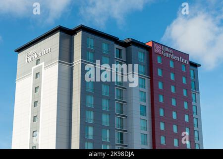 Hilton Garden Inn hotel, a newly constructed, tall building with metal composite panels in grey, red, and light grey against a bright blue sky and clo Stock Photo