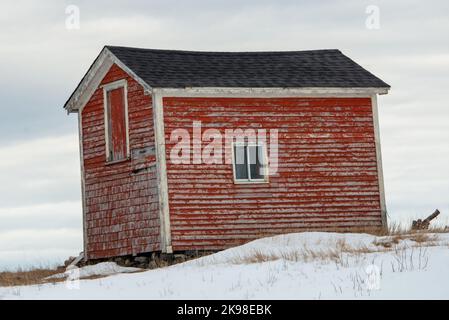A small red wooden barn or shed in the middle of a snow covered field. There's a small hill on which the building sits. There's a hay loft door. Stock Photo