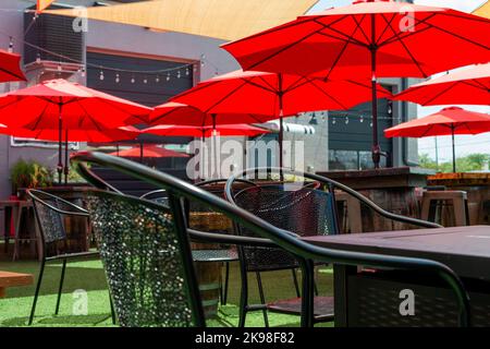 Multiple triangle shaped yellow nylon sunshades and awnings hanging over a patio deck. There are red colored canvas umbrellas hung with strings Stock Photo