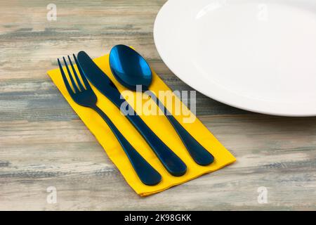 Blue fork knife and spoon on yellow napkin next to white plate Stock Photo